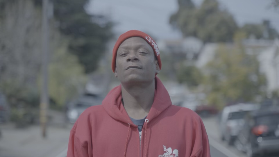 A person in a red hoodie standing on a neighborhood street.