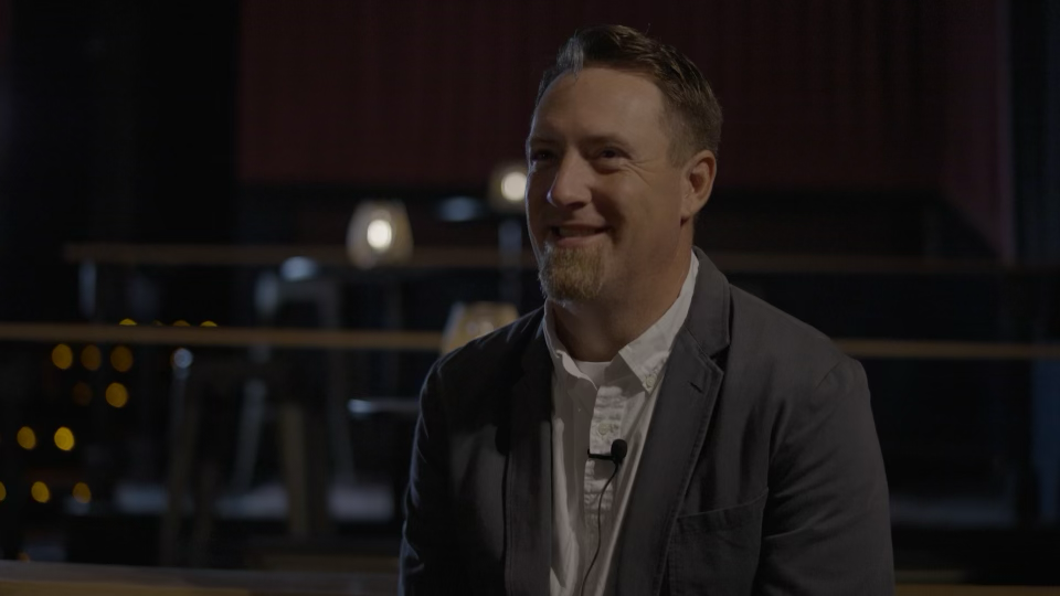 Interview subject in a suit seated in an auditorium.
