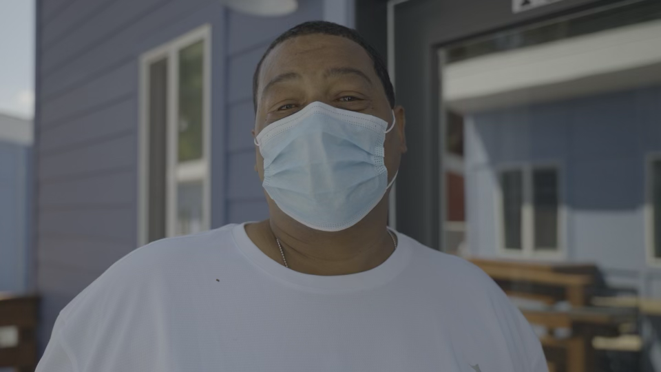 A person in a surgical mask standing outside a home.