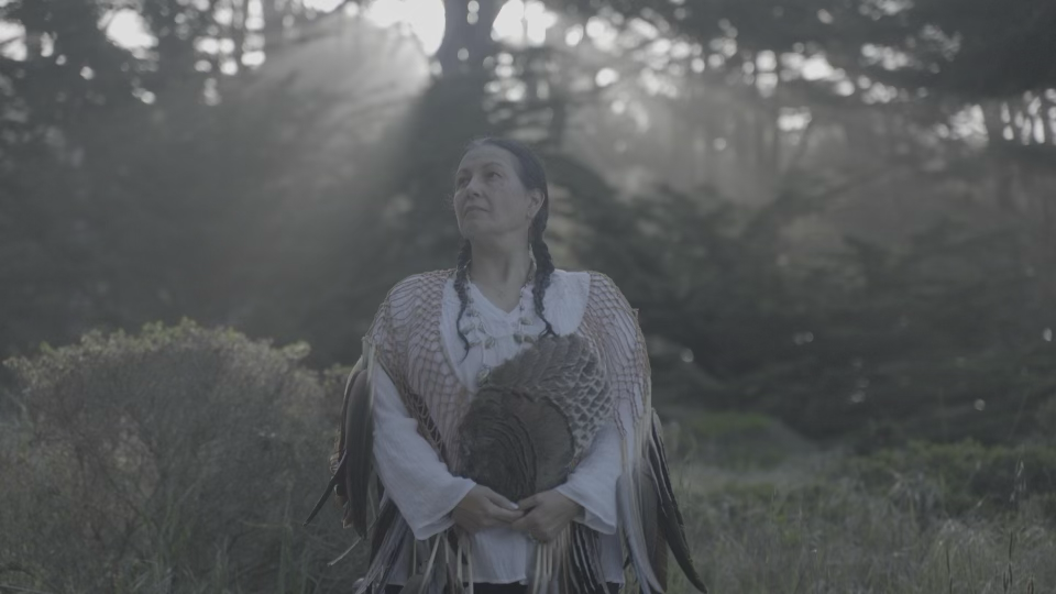 A person outdoors in a shawl, surrounded by trees.