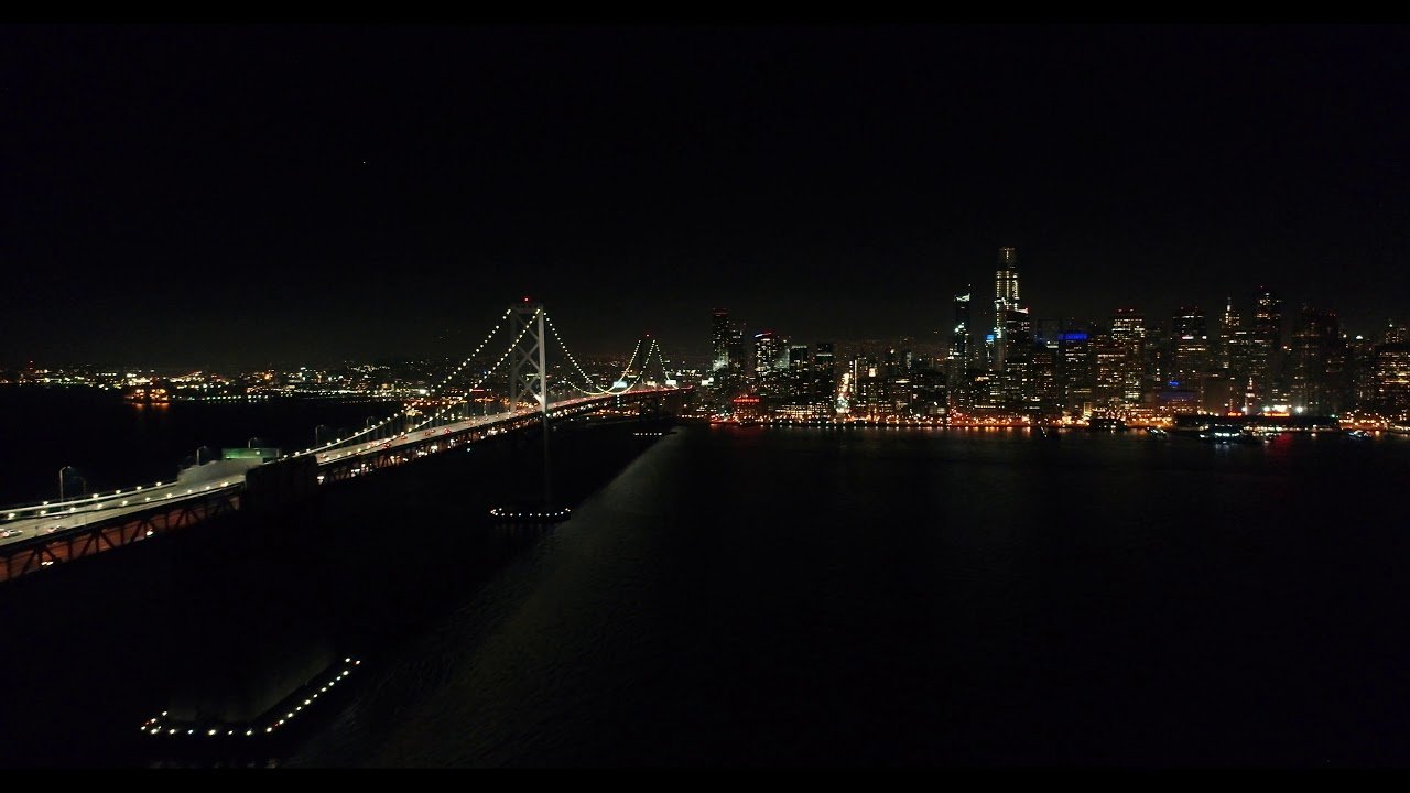 The Bay Bridge and San Francisco skyline illuminated at night.