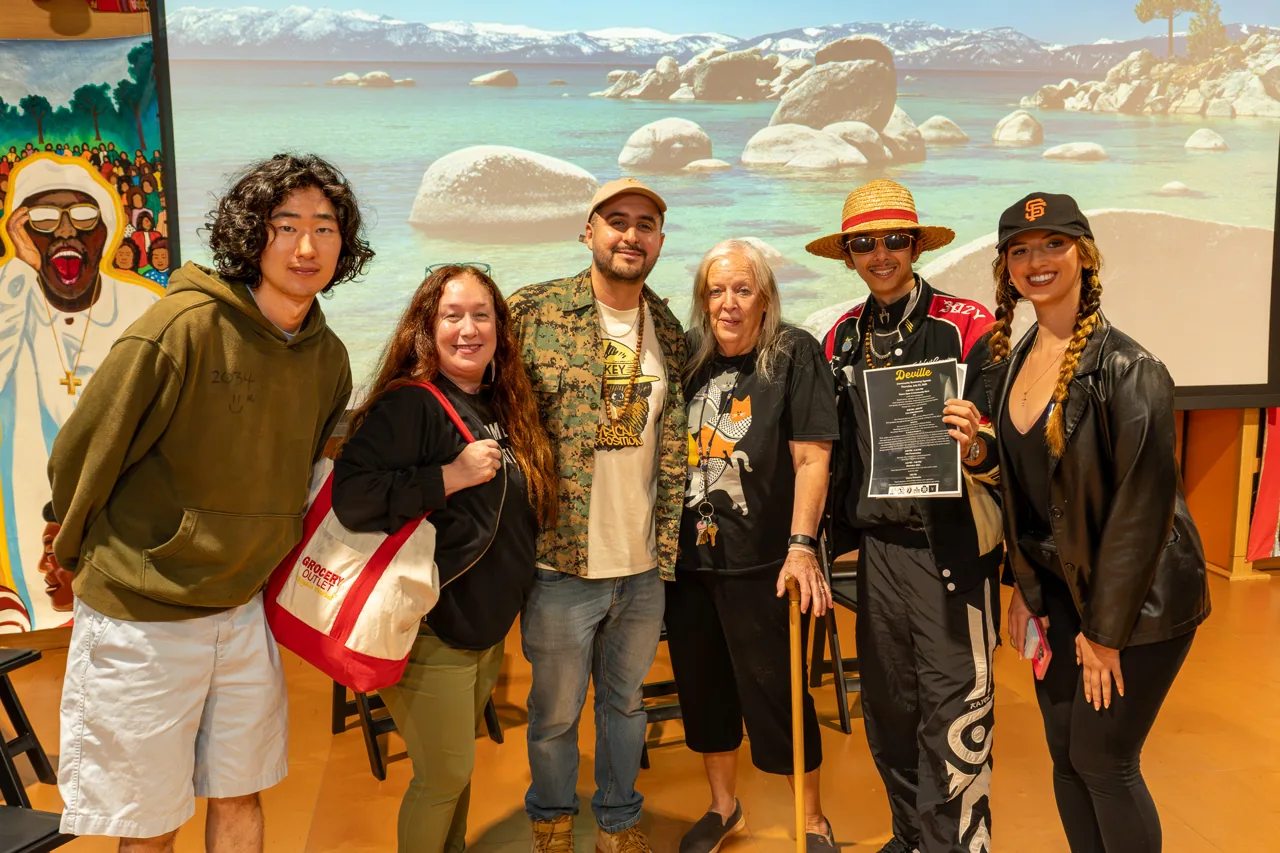 Six people pose together beside artwork and a projected landscape at the Deville community screening.
