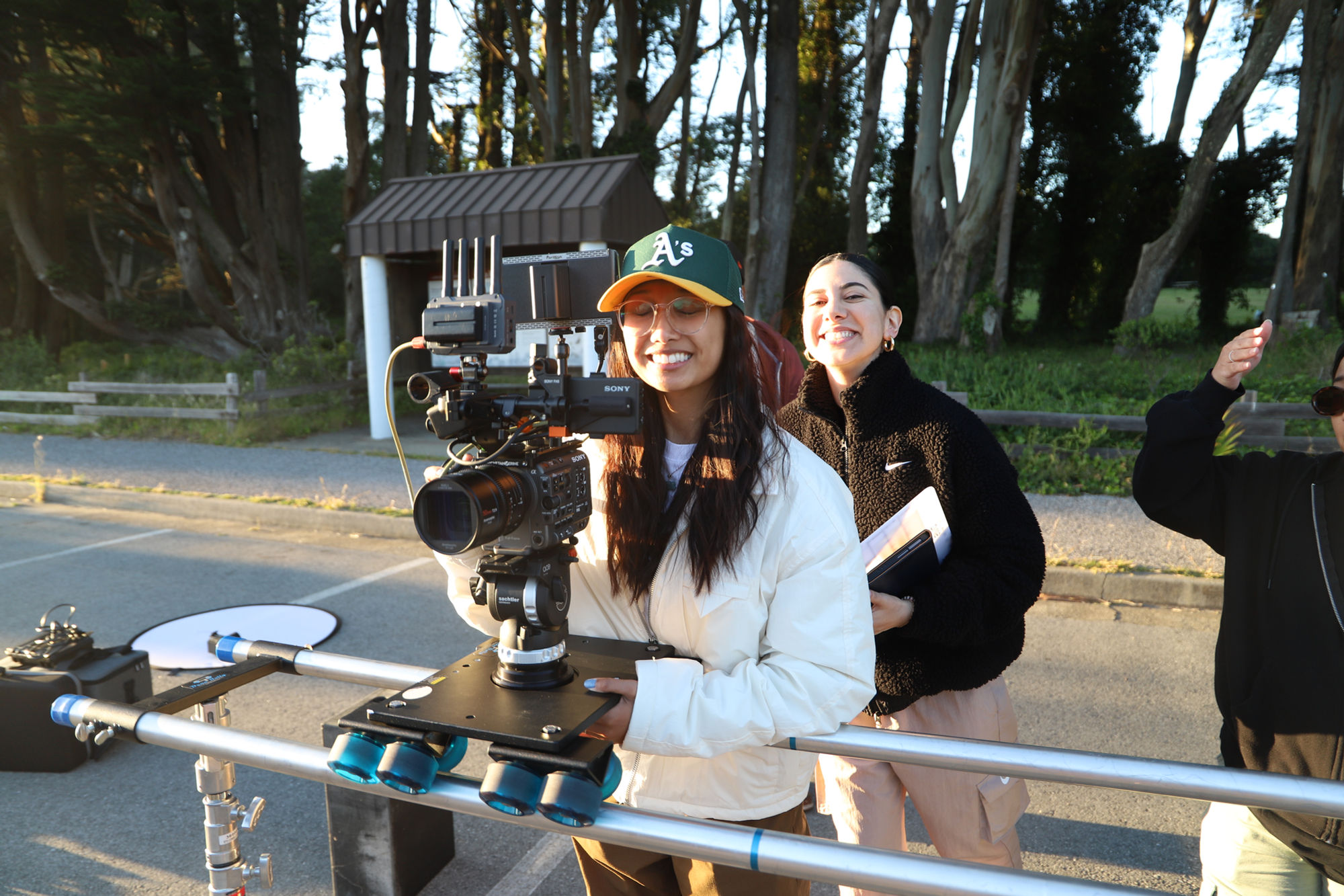 Crew operating a camera on a dolly track along a tree-lined road.