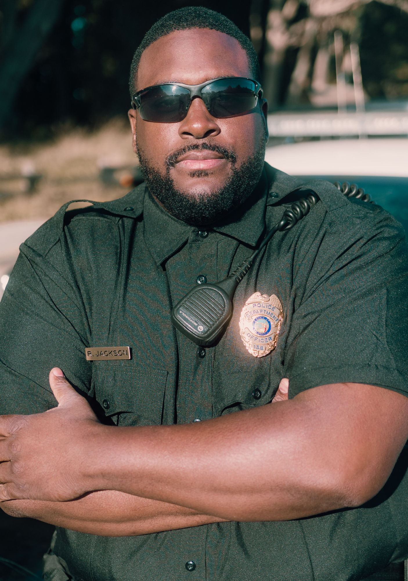 An actor in uniform standing outdoors with his arms crossed.