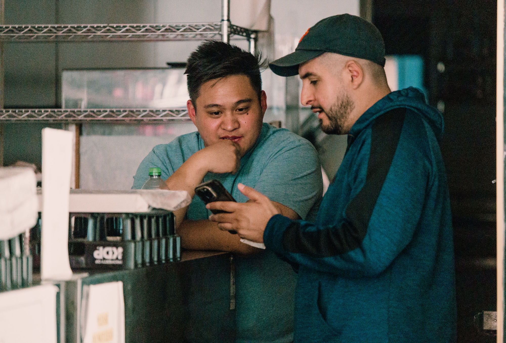 Two crew members with a camera in a corner store stockroom.