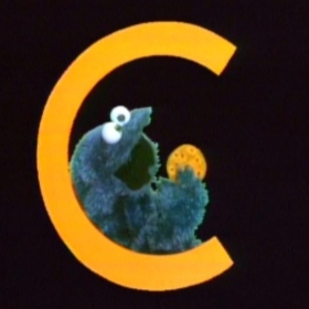 The Cookie Monster from Sesame Street sitting in a giant letter 'C' eating a cookie.