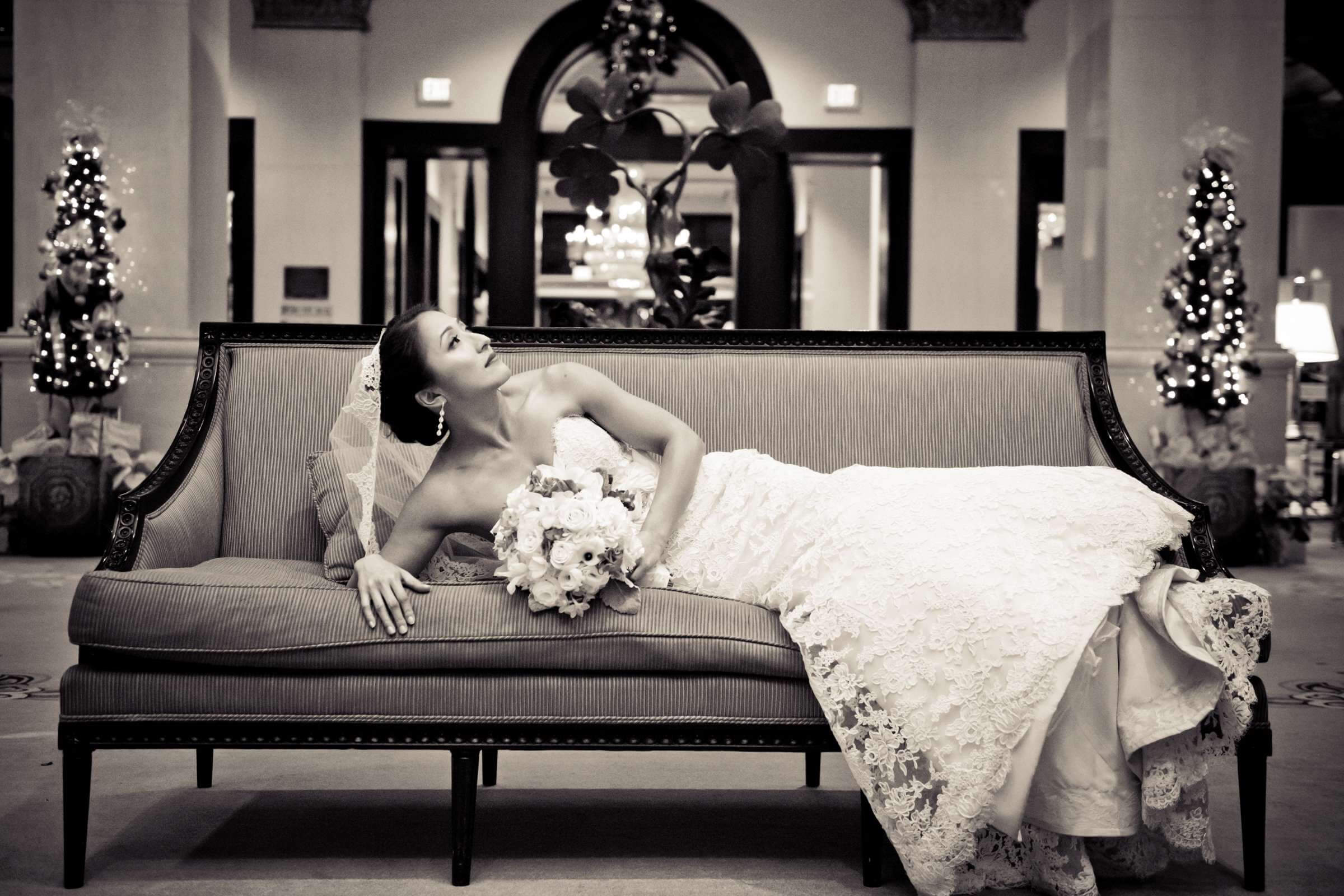 Bride reclining on a sofa in a wedding gown with a polished updo and makeup