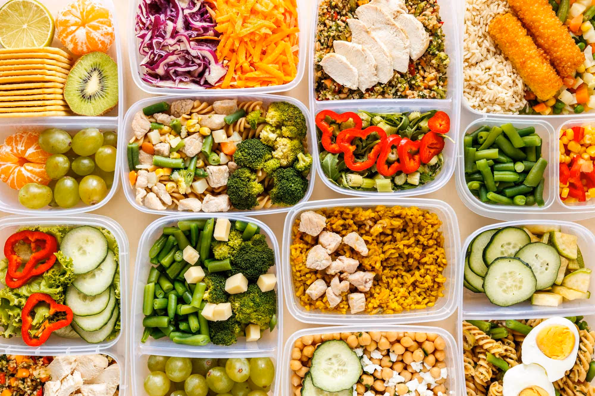 Assorted healthy meal prep containers filled with fruits, vegetables, grains, and sliced meats arranged neatly.