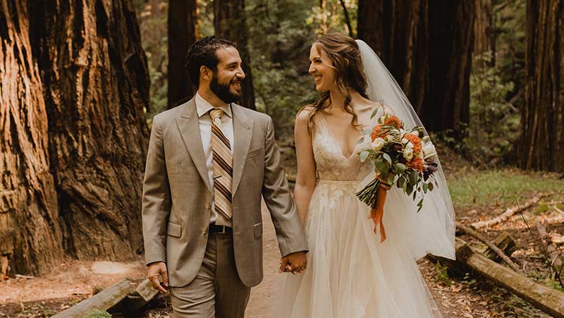 newly married couple walking through the redwood forests smiling at each other