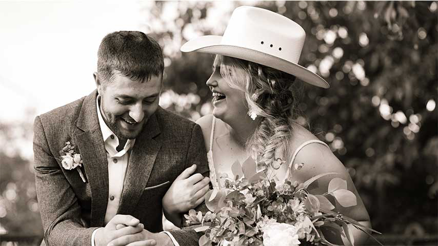 Bride laughing while wearing grooms cowboy hat as they embrace