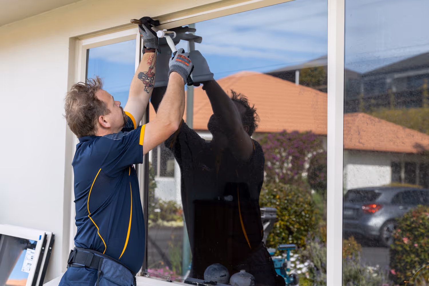 Man wearing gloves installing or repairing a window on a house exterior during the daytime.
