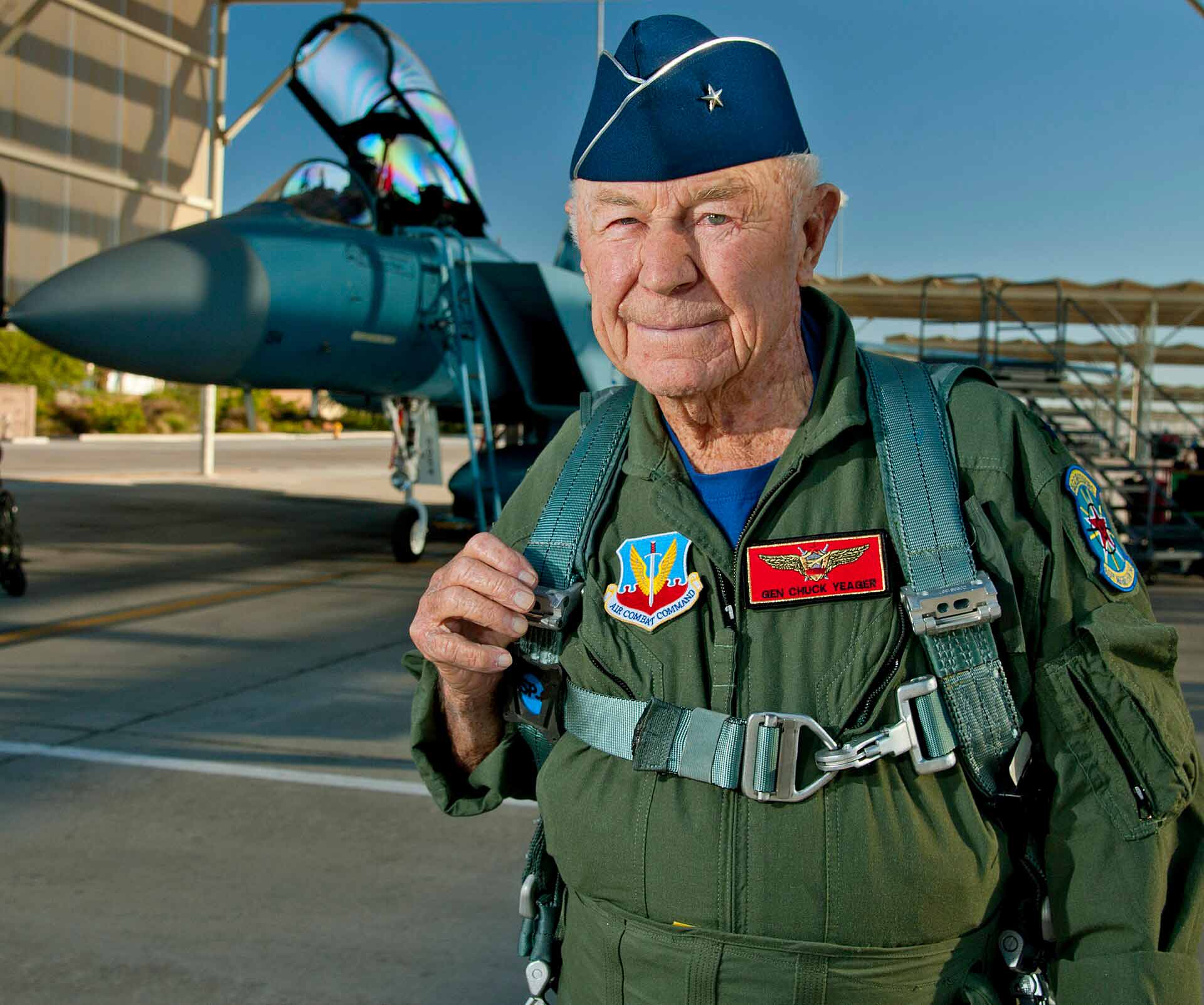 An elderly person in military flight-gear, stood in from of an aircraft.