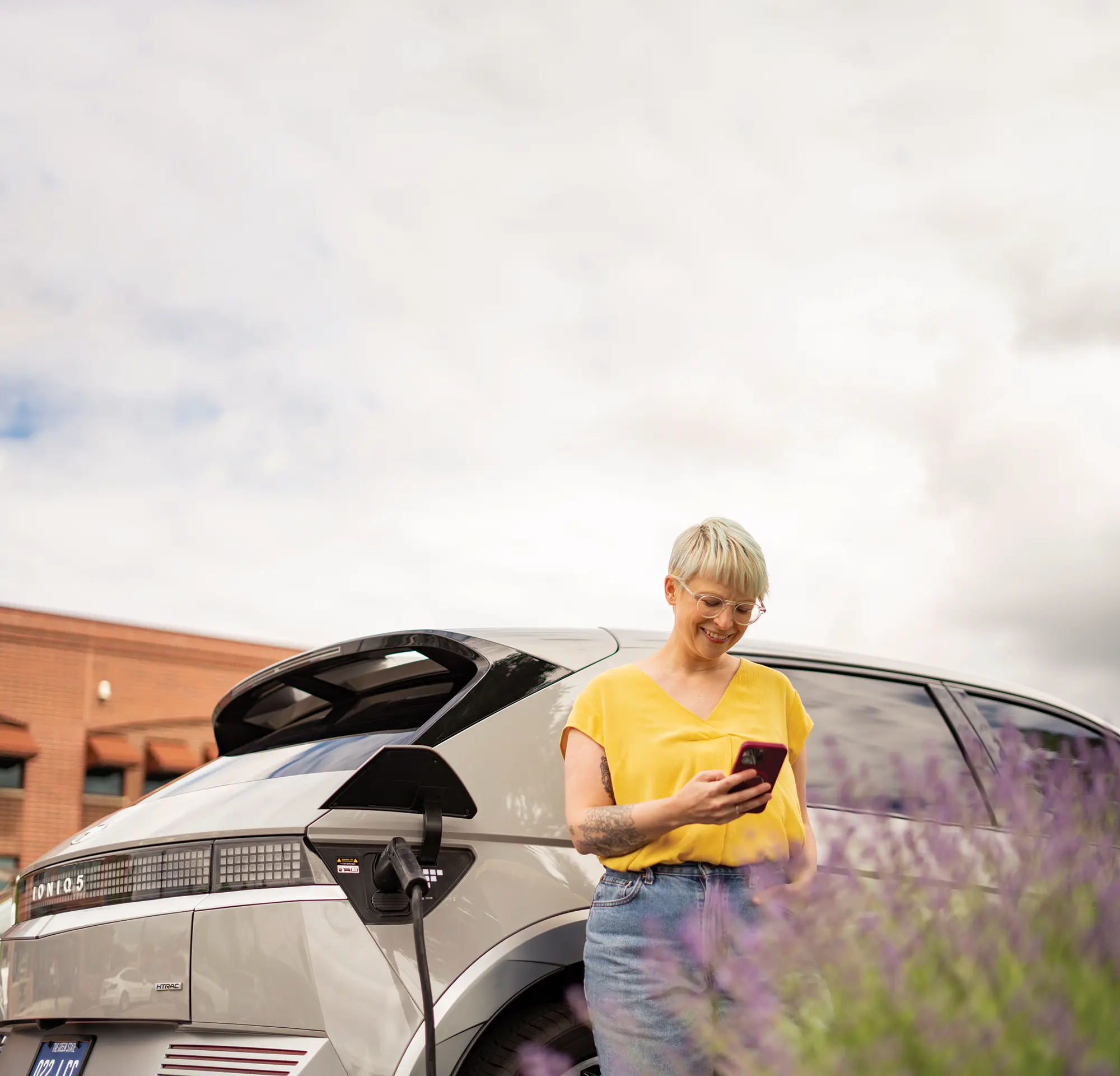 Woman learning about ev's and electric cars on her phone next to a Hyundai IONIQ5