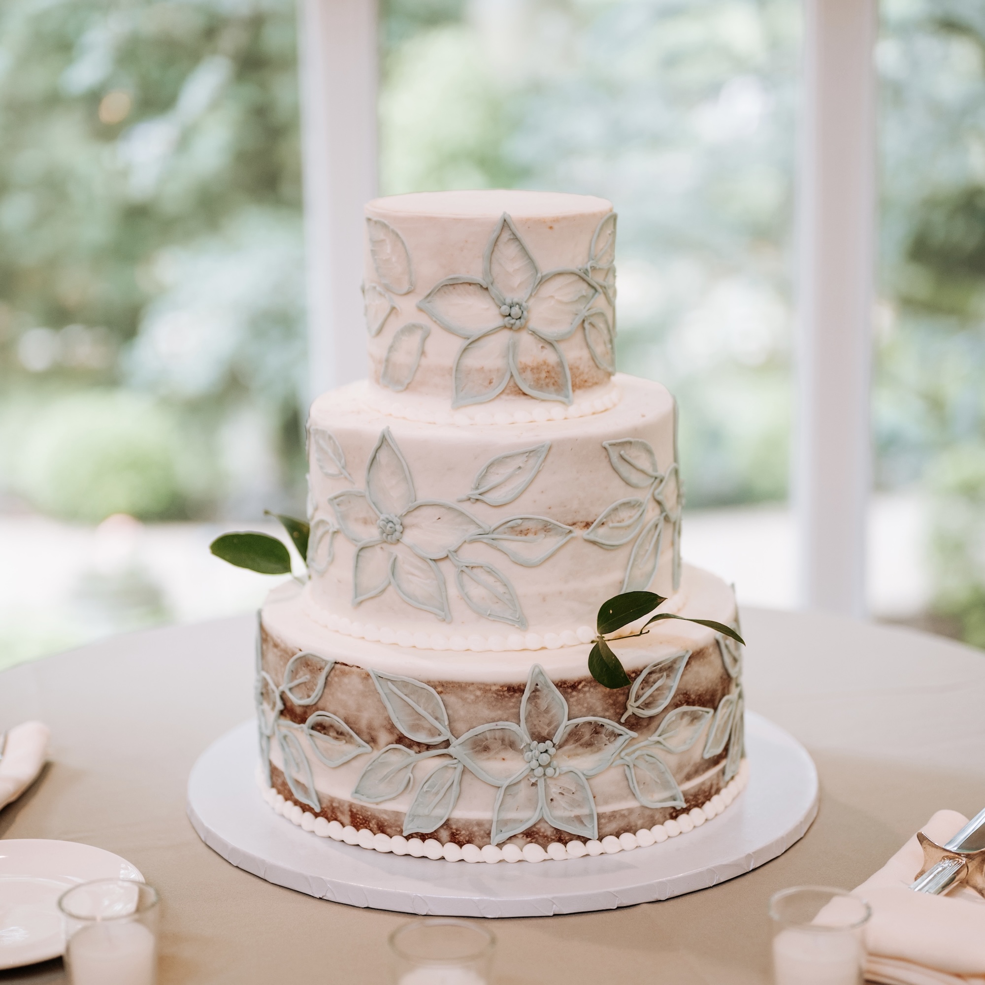 A custom wedding cake with decorative flowers on the icing, on display in the window at Pomme Radnor overlooking the woodland