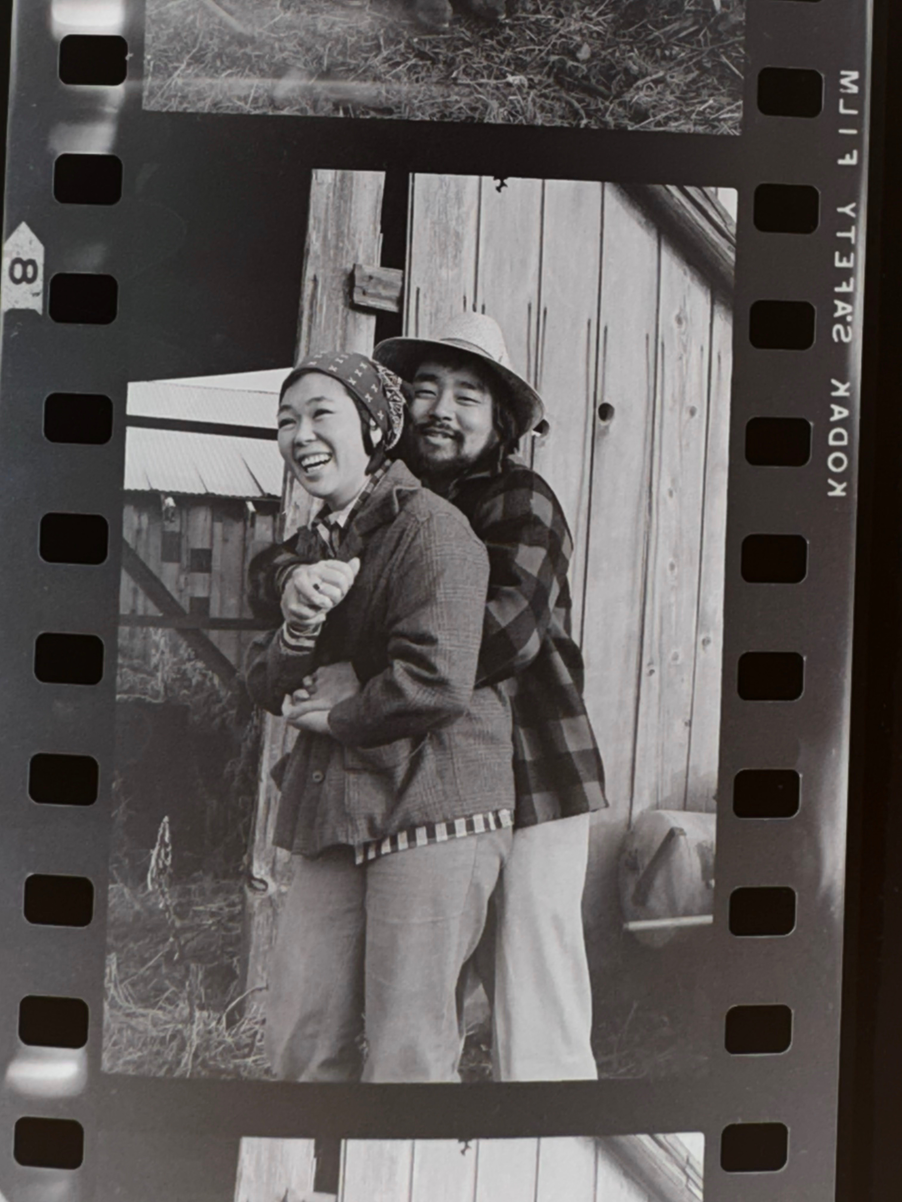 Two cast members embrace and laugh in front of a weathered wooden barn door. Gold Watch, 1977. Photo by Steve Suzuki.