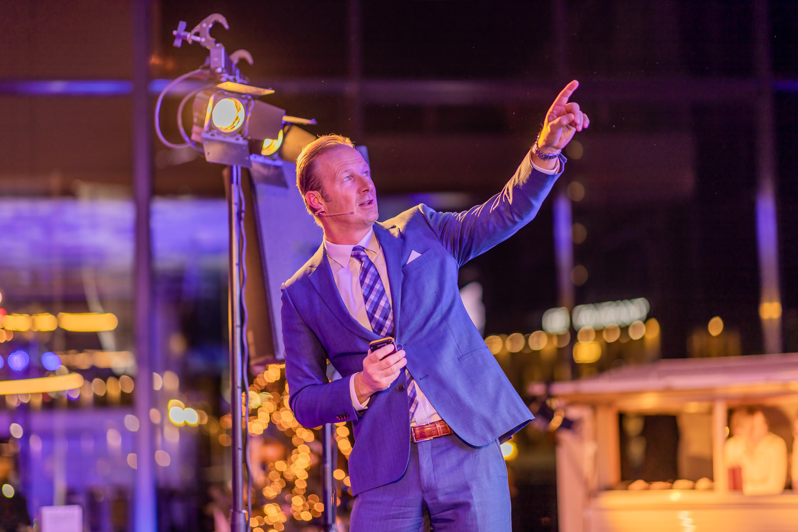 Two men in white shirts holding large arrow signs labeled 'HOPE' and 'NaaS' inside a spacious, industrial-style event space with pink and purple lighting and groups of people socializing.