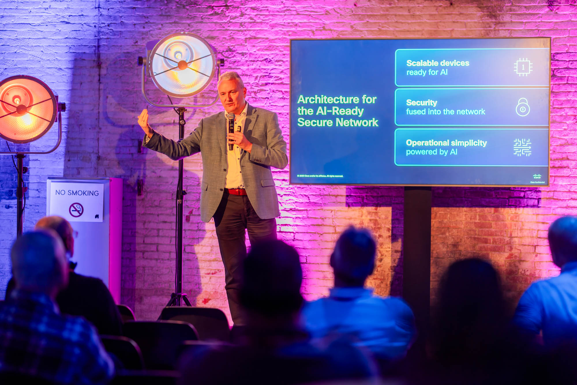 Two men in white shirts holding large arrow signs labeled 'HOPE' and 'NaaS' inside a spacious, industrial-style event space with pink and purple lighting and groups of people socializing.