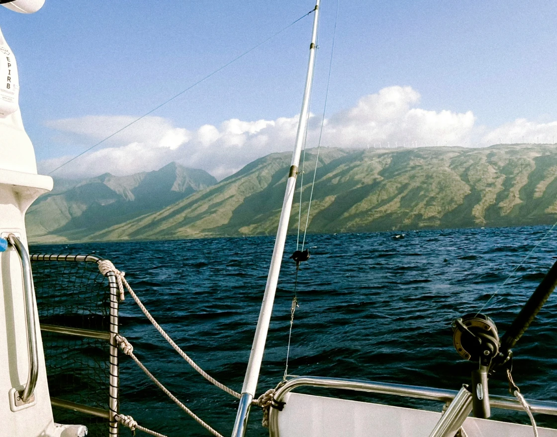 Person fishing from the front of a boat named The Fish Tank on calm open water under a clear sky.