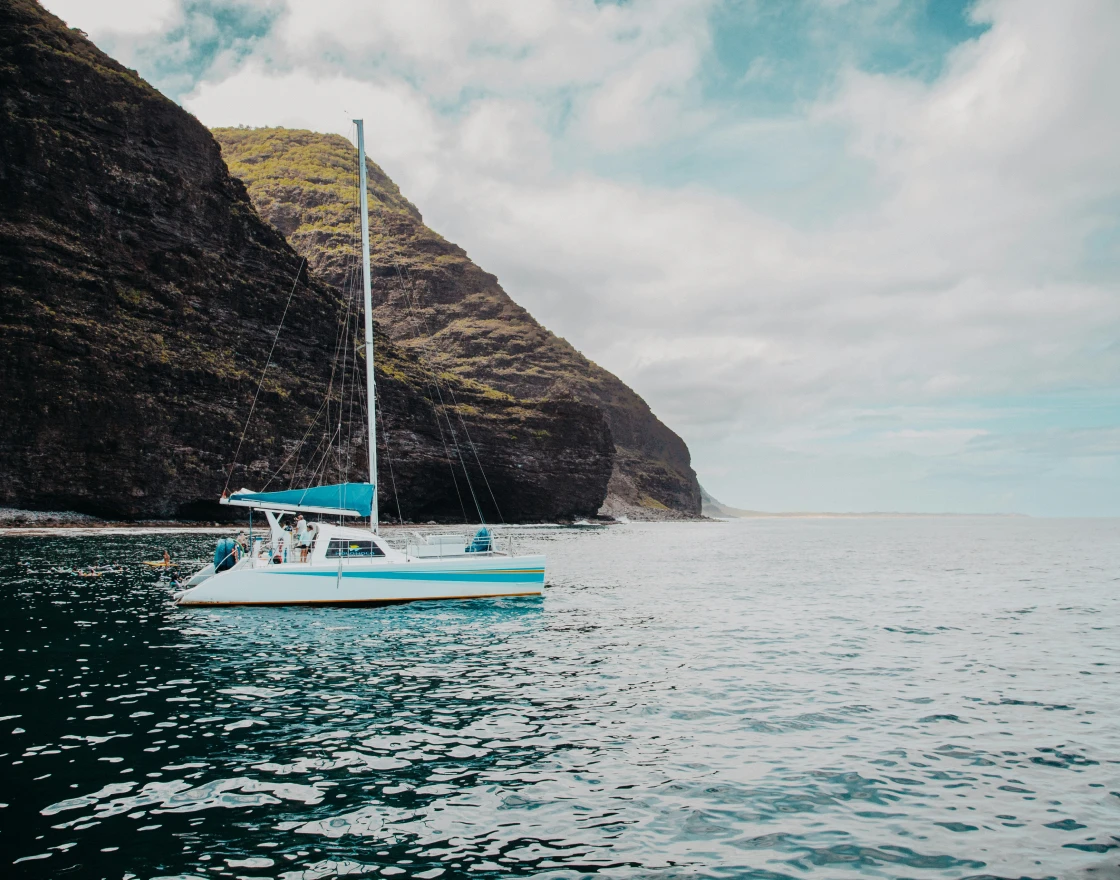 Person fishing from the front of a boat named The Fish Tank on calm open water under a clear sky.