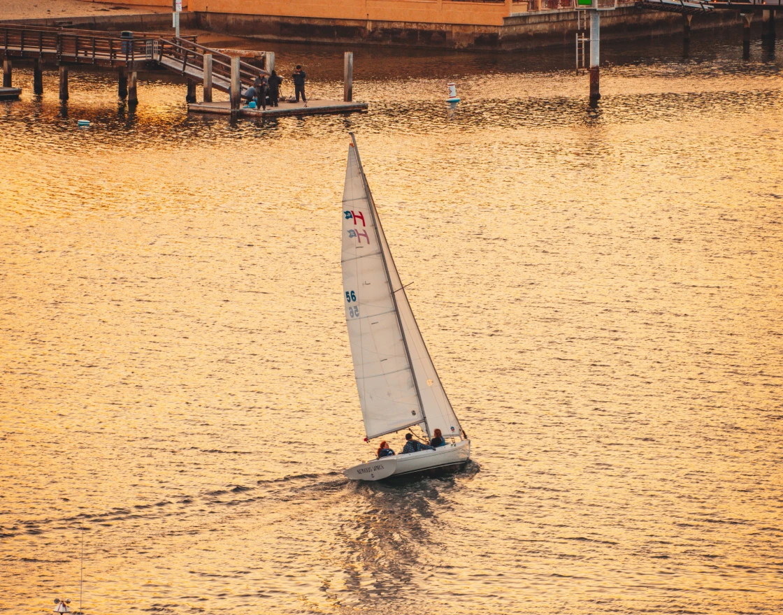 Person fishing from the front of a boat named The Fish Tank on calm open water under a clear sky.