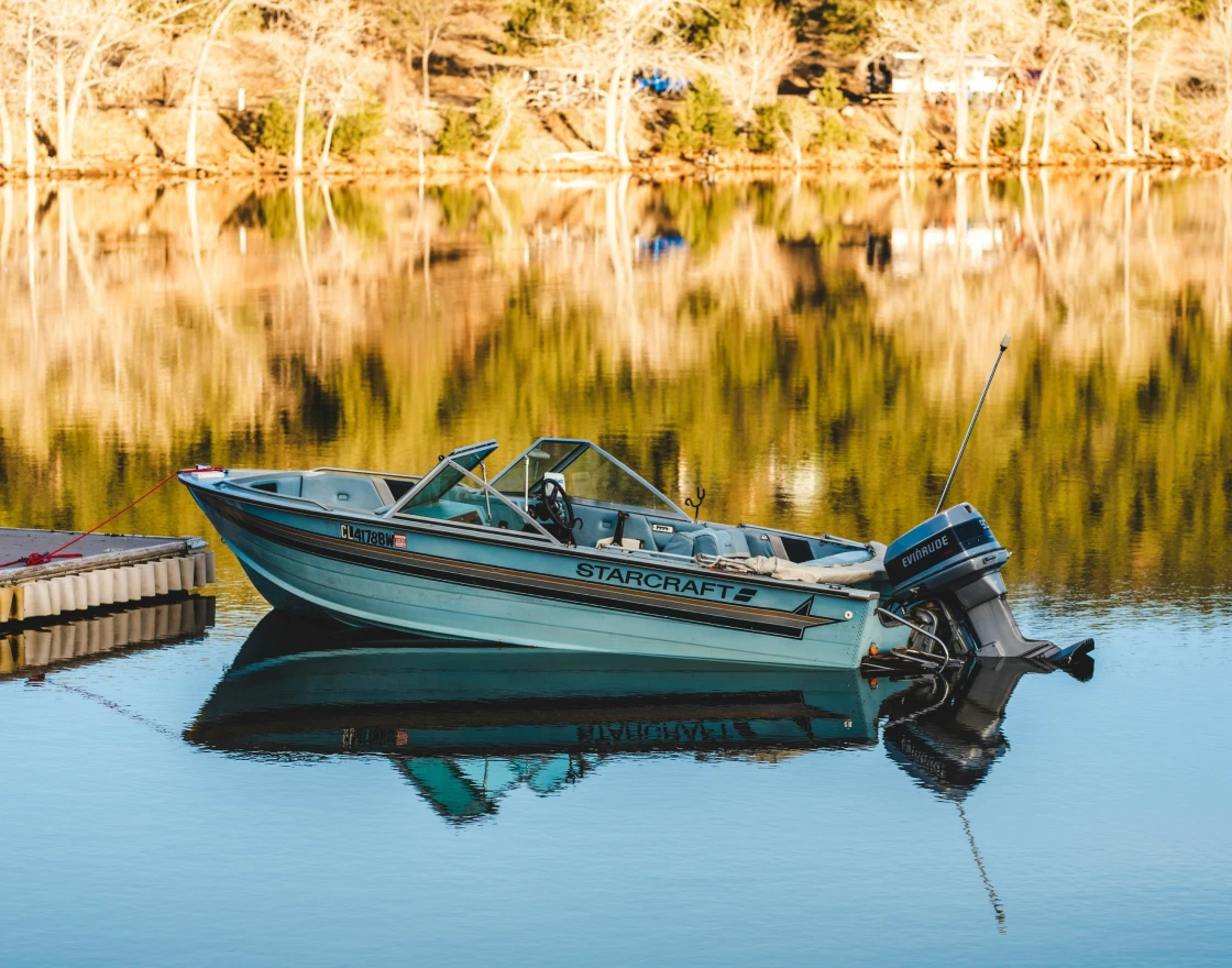 Person fishing from the front of a boat named The Fish Tank on calm open water under a clear sky.