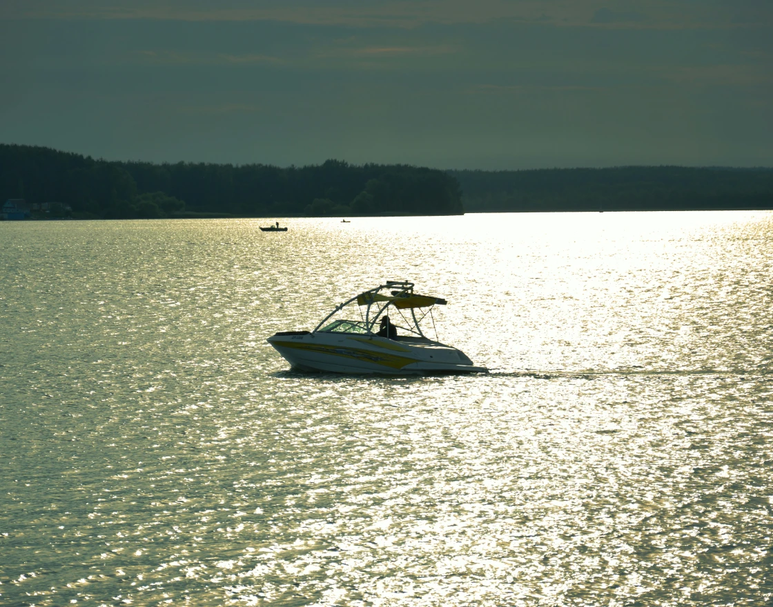 Person fishing from the front of a boat named The Fish Tank on calm open water under a clear sky.