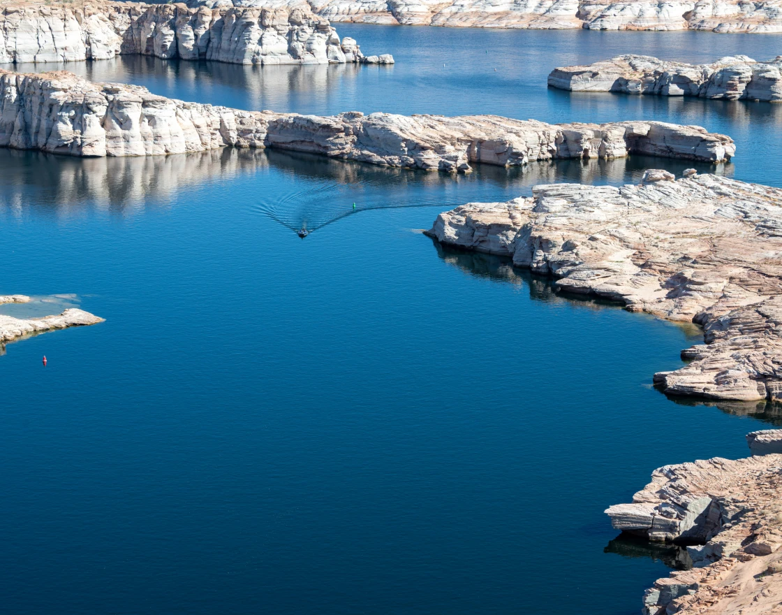 Person fishing from the front of a boat named The Fish Tank on calm open water under a clear sky.