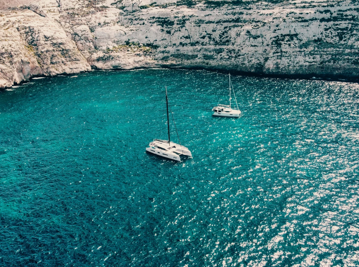 Pontoon boat with several people cruising on calm ocean water under a clear sky.