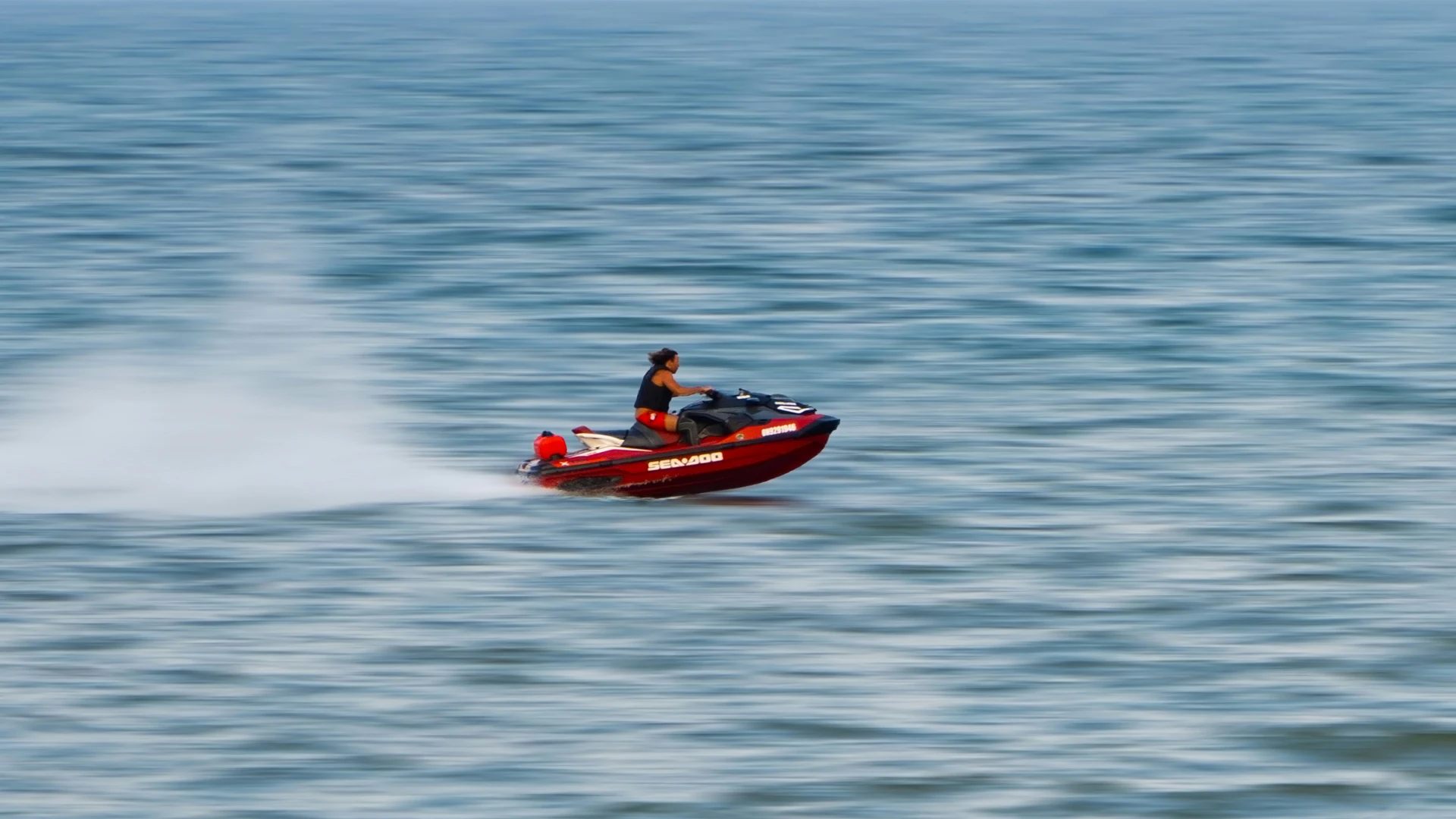 Person fishing from the front of a boat named The Fish Tank on calm open water under a clear sky.