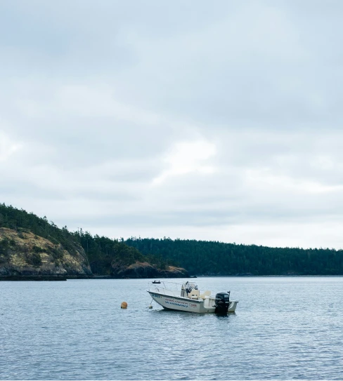 Person fishing from the front of a boat named The Fish Tank on calm open water under a clear sky.