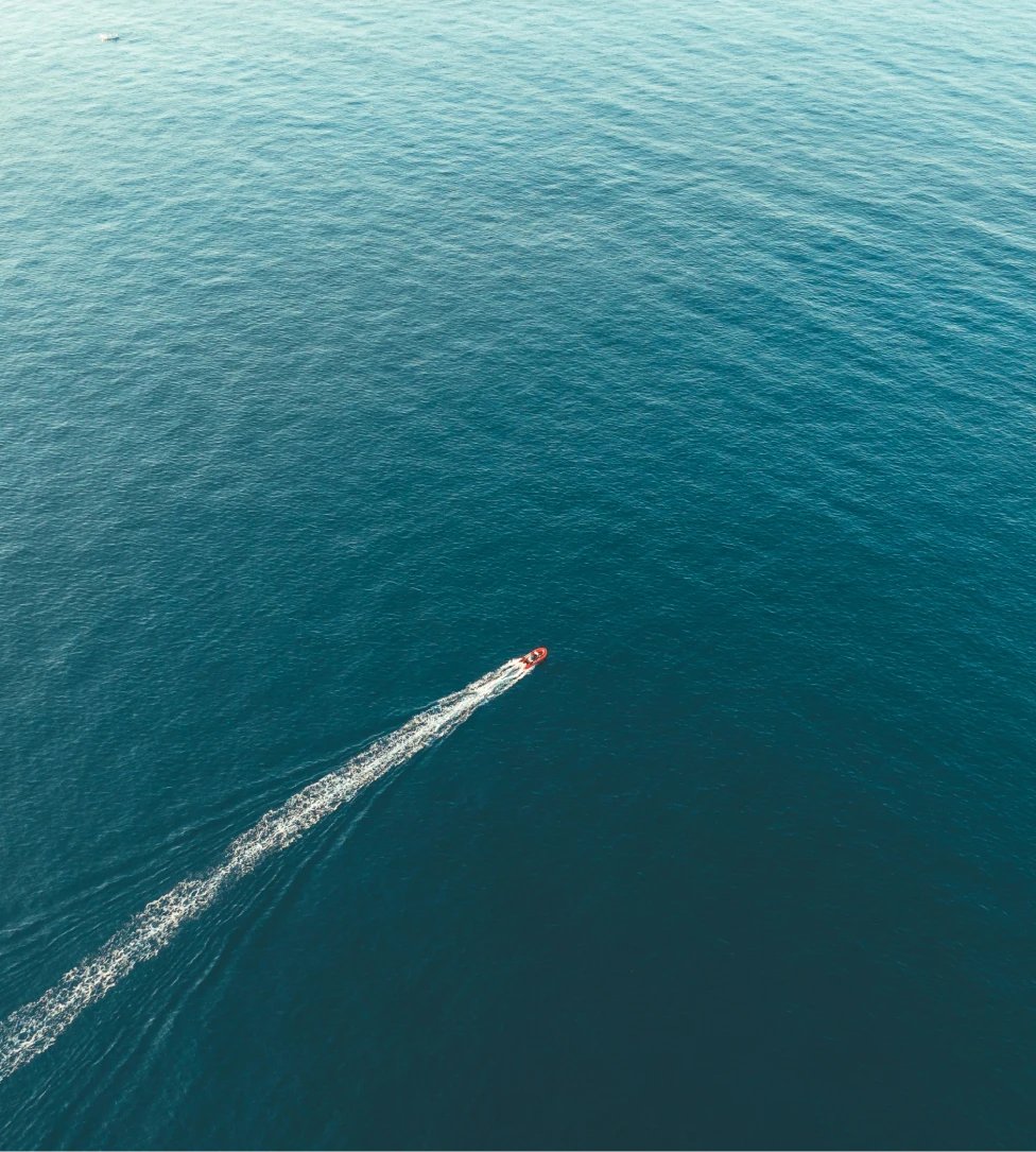 Person fishing from the front of a boat named The Fish Tank on calm open water under a clear sky.