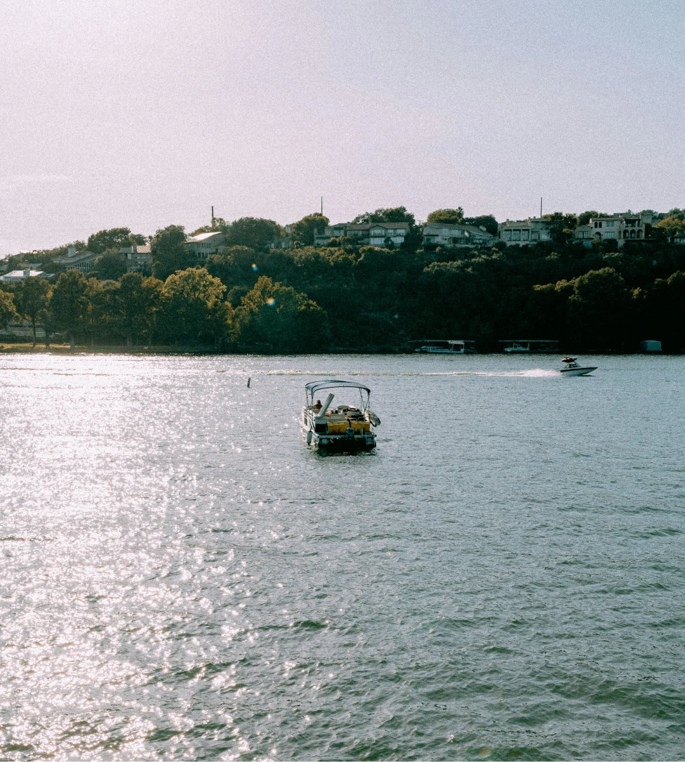 Person fishing from the front of a boat named The Fish Tank on calm open water under a clear sky.