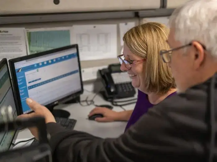 A smiling woman looking at a what a man is pointing at on the computer screen.