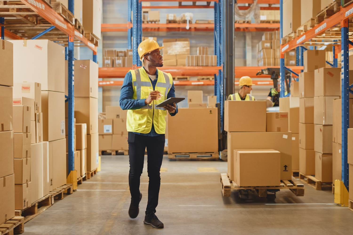 A warehouse distribution center worker walking around the warehouse floor with a clipboard checking inventory