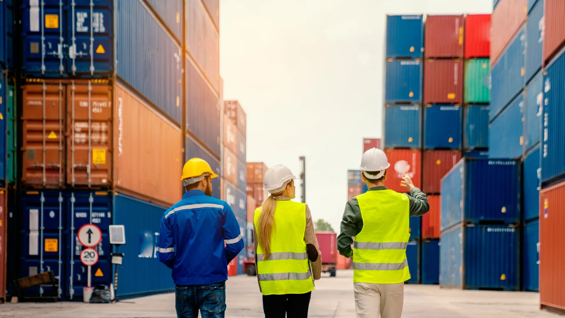 Three people standing and talking with stacked, colorful containers on either side of them.