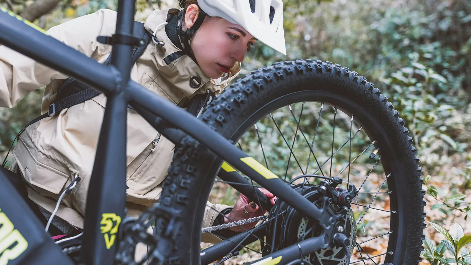 A women inspecting her e-bike while out on a trail