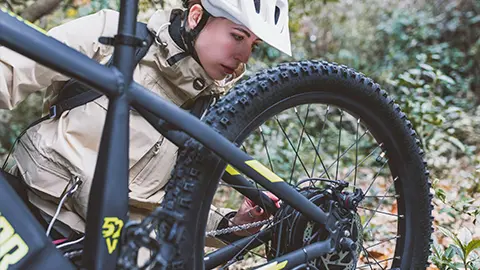 A women inspecting her e-bike while out on a trail