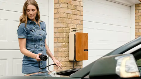 A women charging her EV vehicle at home on a sunny day