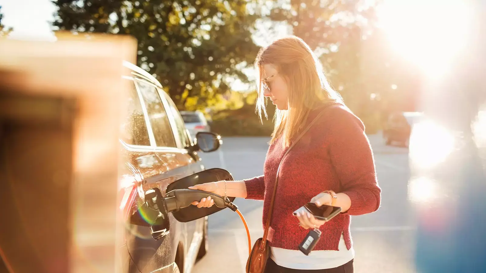 Woman charging an EV car in bright afternoon sunlight