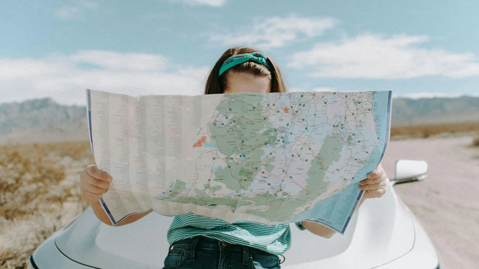 chica sosteniendo un mapa en busca de estaciones de carga de hidrógeno frente a su coche