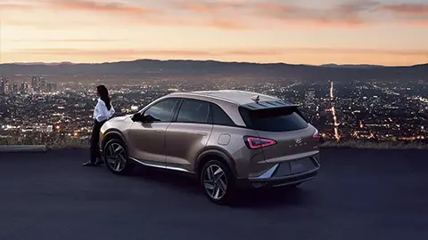 imagen de una mujer apoyada en el Hyundai Nexo con vistas a una ciudad