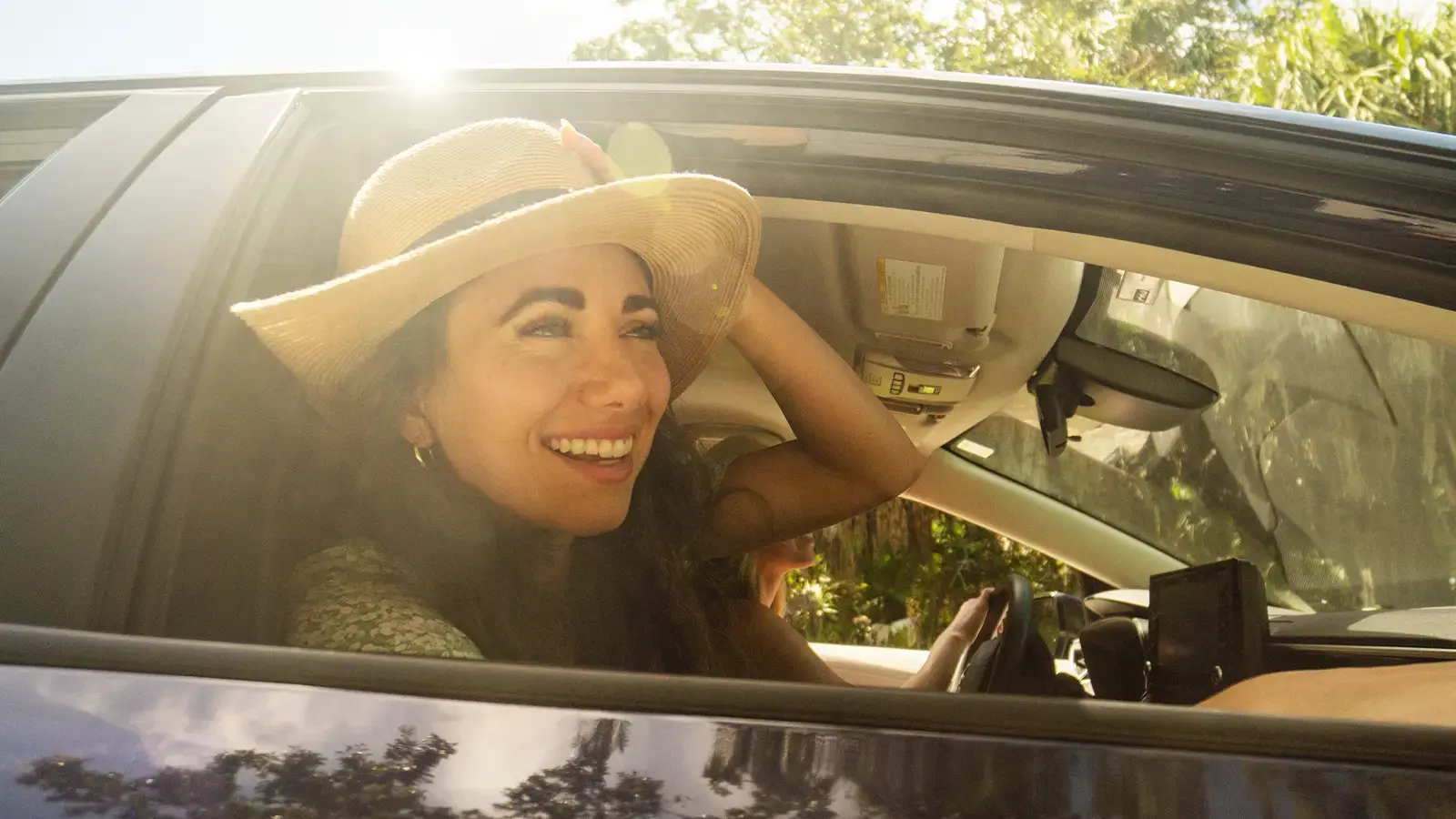 mujer sonriente montando en un coche verde con las ventanillas bajadas y el viento soplando