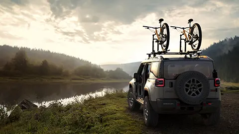 A silver 2026 Jeep Recon EV with bikes on top in a scenic river
