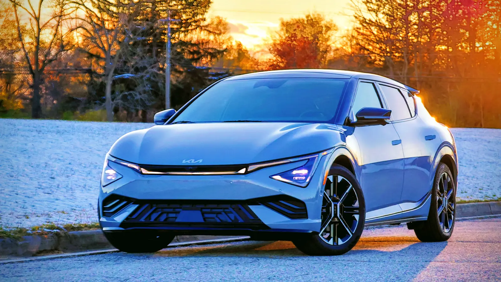 A white Kia EV6 in a snowy forest at sunset