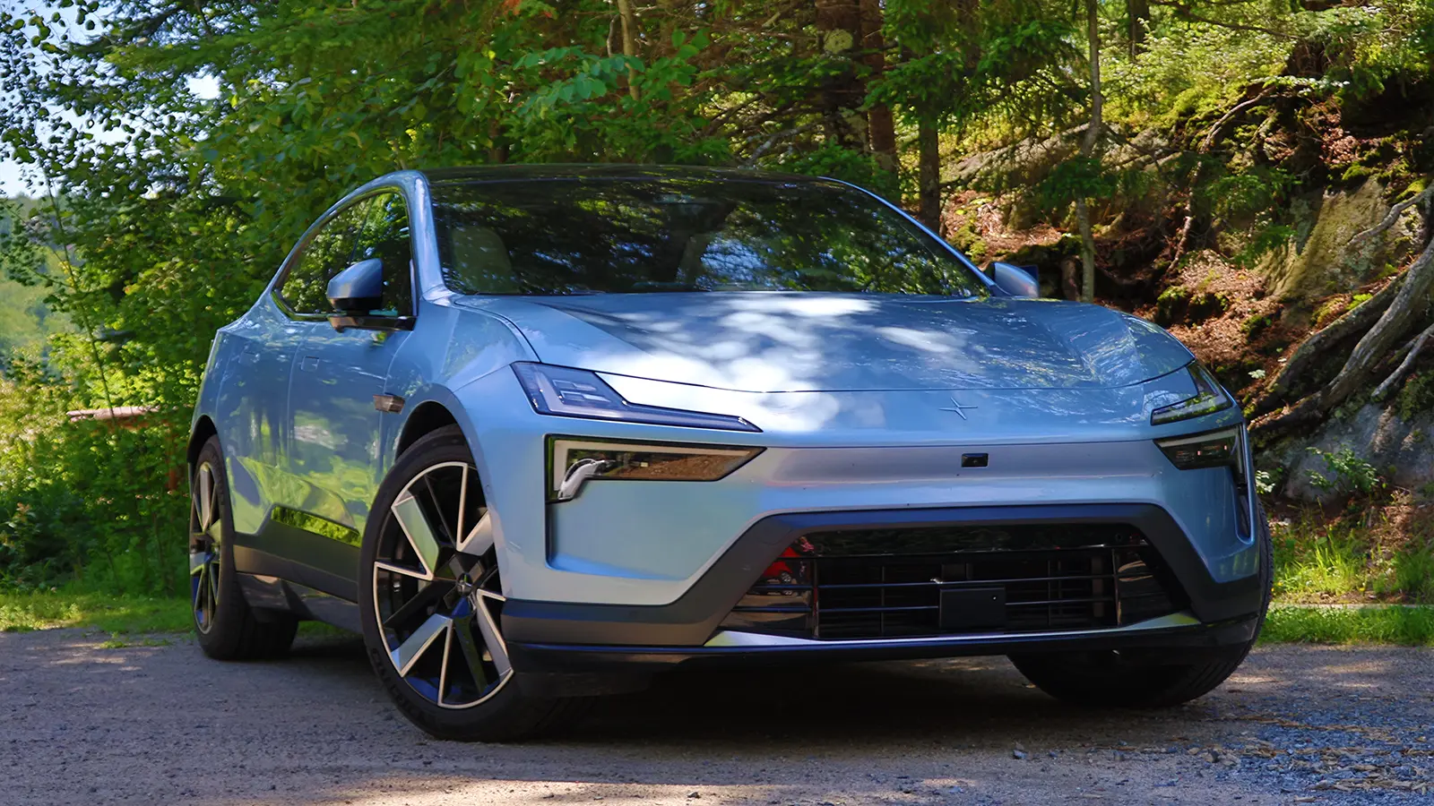 A silver Polestar 4 in the green forest on a bright summer day