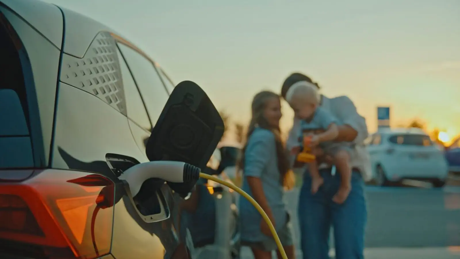 Una familia feliz en primer plano en la playa mientras se carga un vehículo eléctrico
