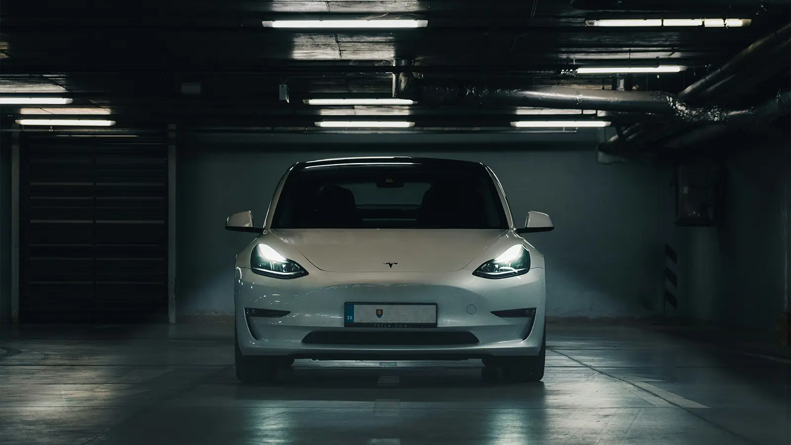 Un Tesla Model S blanco en un estacionamiento oscuro con los faros encendidos
