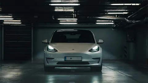 Un Tesla Model S blanco en un estacionamiento oscuro con los faros encendidos