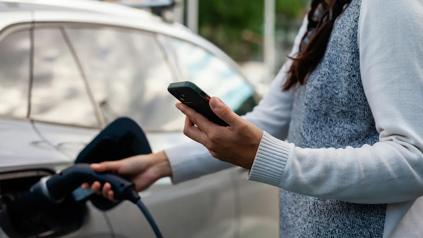 Una mujer carga su vehículo eléctrico bajo la luz del sol de la tarde