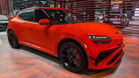 A 2027 orange Genesis GV60 Magma three quarter front view